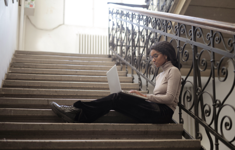 A woman sat on the stairs holding a laptop