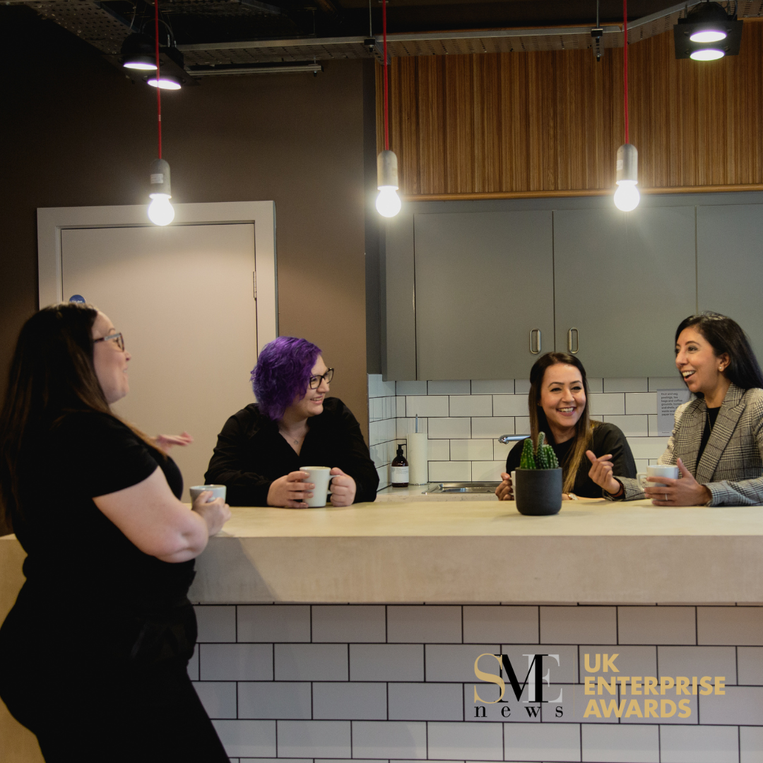 A group of women stood around an office kitchen counter with the SME UK Enterprise Awards logo