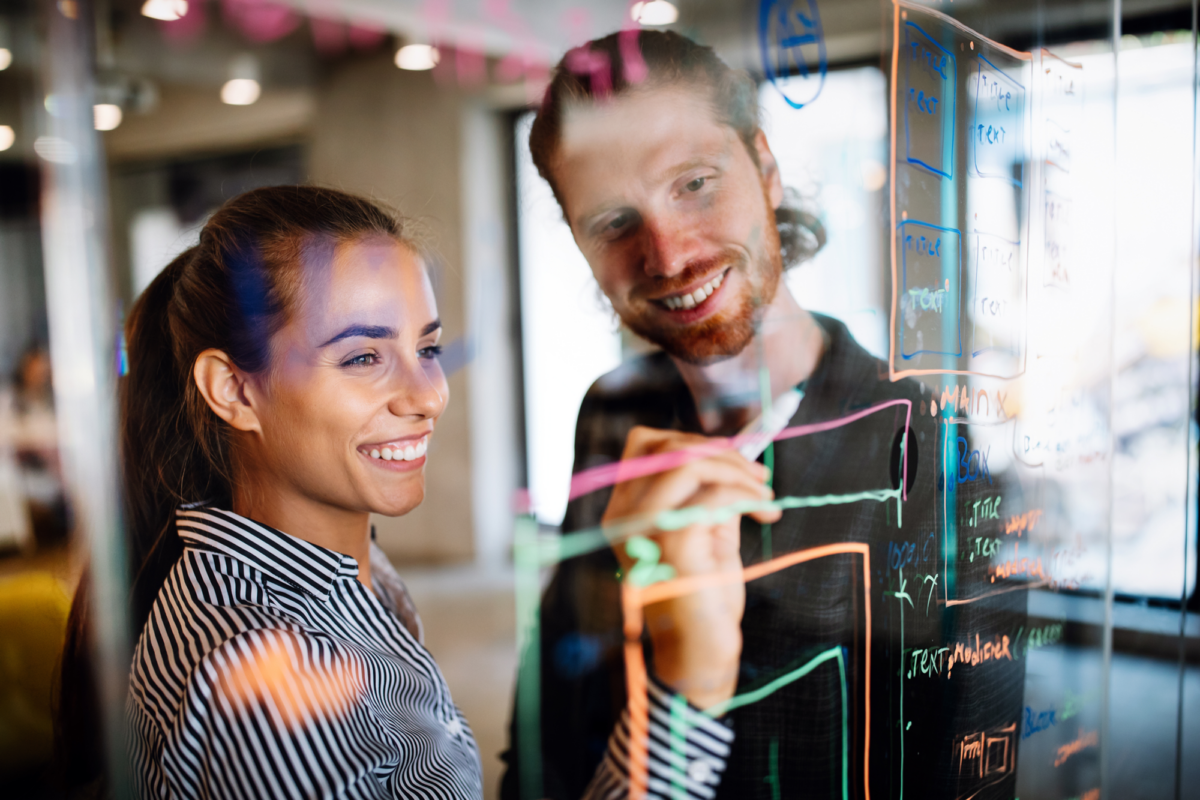 A man and a woman working on a transparent whiteboard