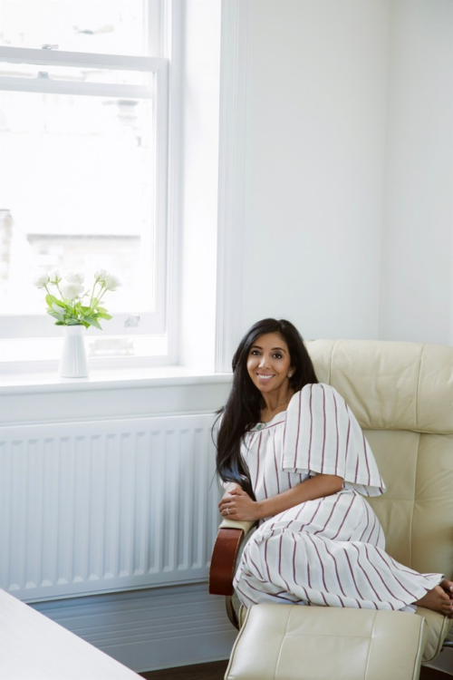 Leena Parmar lounging in a large chair in a white dress with black stripes
