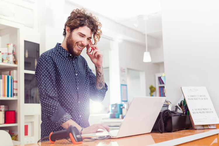 A man on a phone stood at a desk on the phone while on a laptop