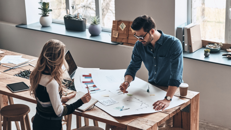 A man and a woman drawing a large chart on a table