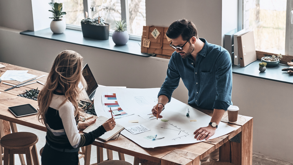 A man and a woman drawing a large chart on a table