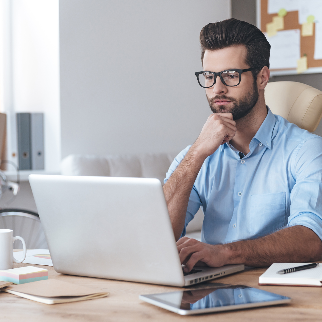 A man sat at a desk looking at a laptop