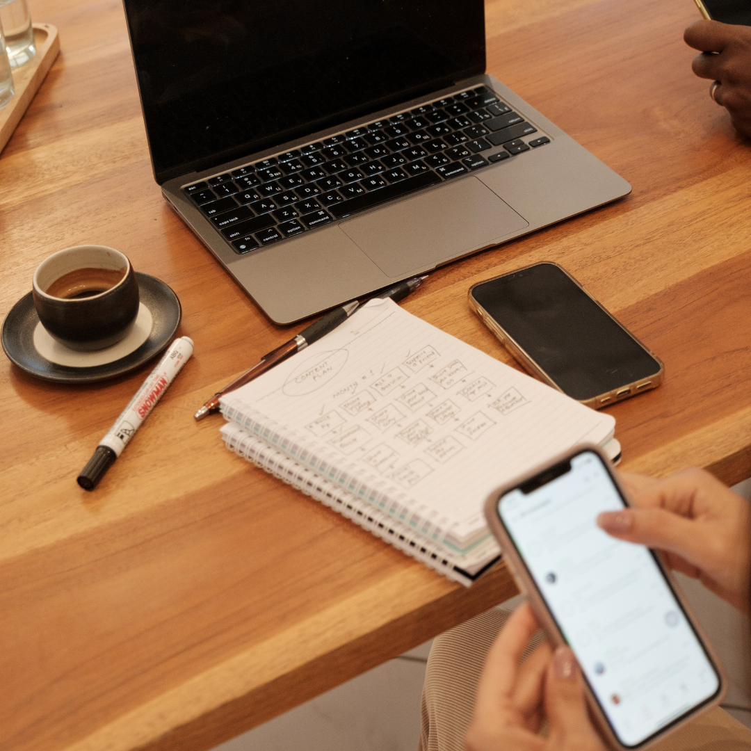 A table set with a laptop, phone, notebook, pen, marker, and teacup