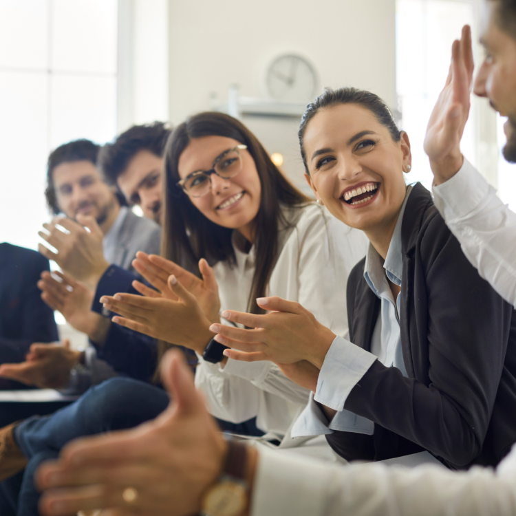 A group of professionals sat down clapping and smiling.