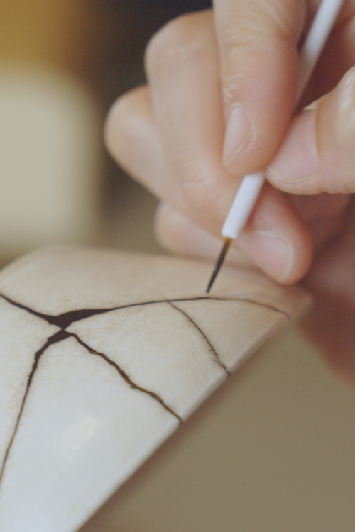 A close-up of a beautifully repaired ceramic piece where the cracks are filled with gold lacquer, highlighting the repair as a beautiful and strong part of the object.