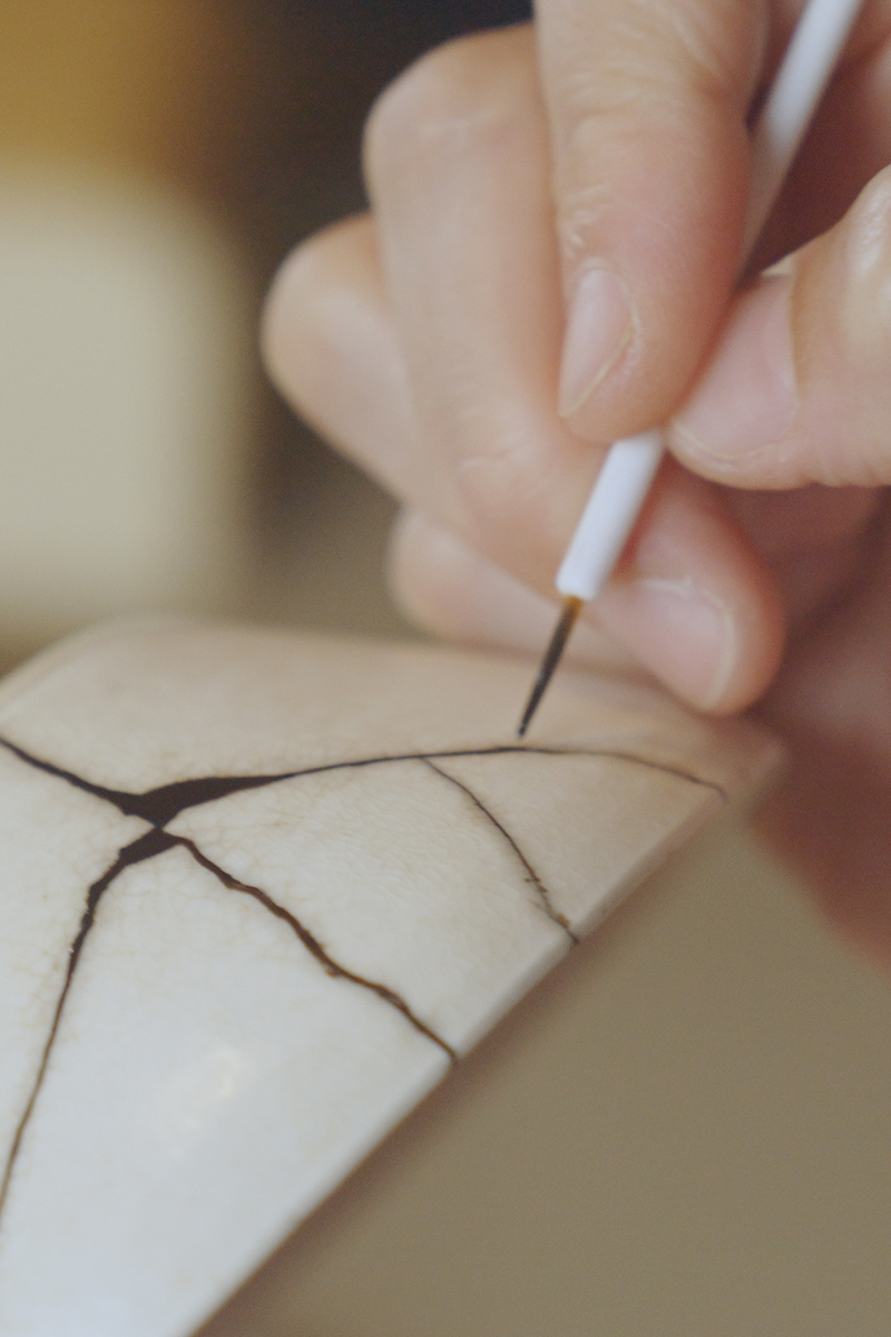 A close-up of a beautifully repaired ceramic piece where the cracks are filled with gold lacquer, highlighting the repair as a beautiful and strong part of the object.