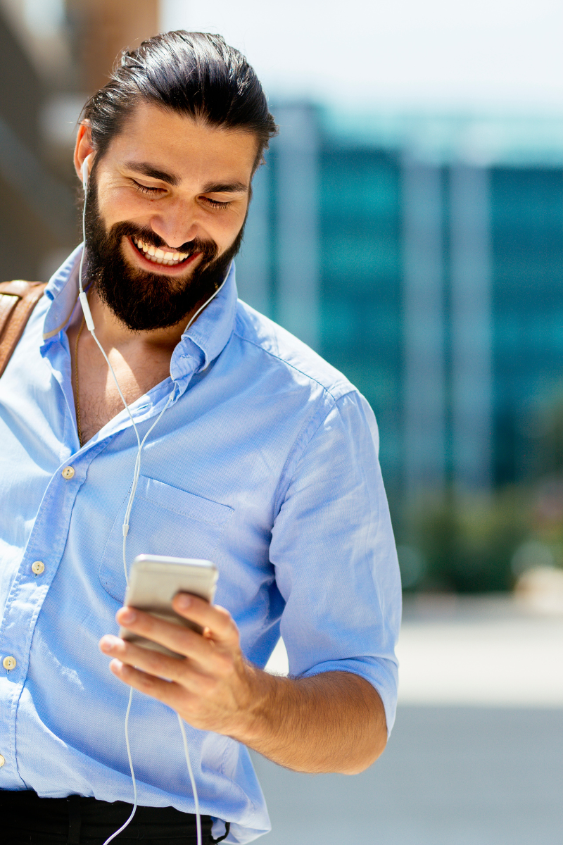A man smiling outside looking at his phone.
